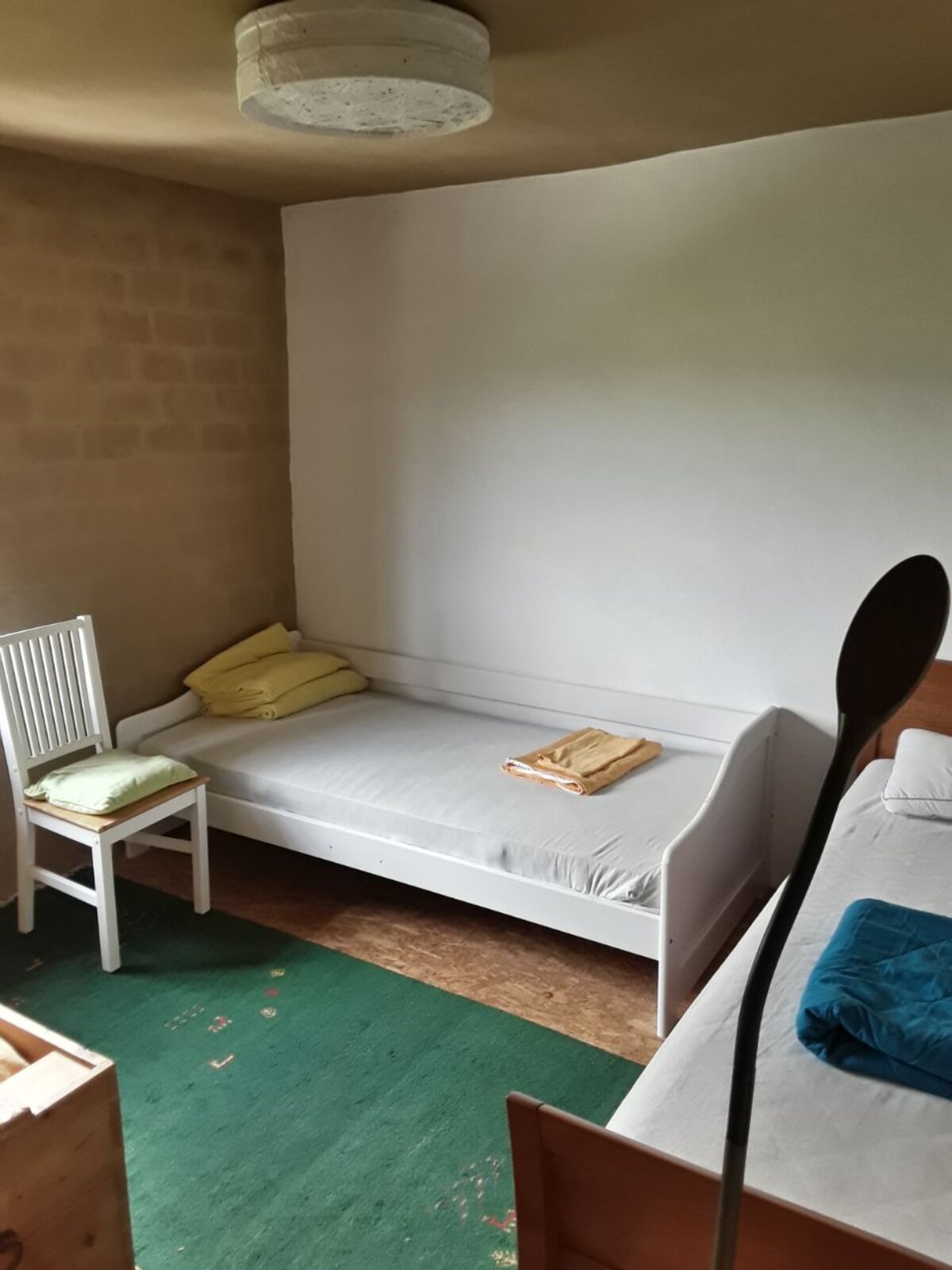 Ein Zimmer für die Auszeit — einfaches Bett, grüner Teppich, Licht vom Fenster